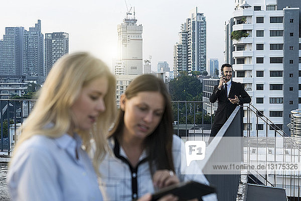 Businessman speaking on smartphone while female colleagues looking into tablet on city rooftop