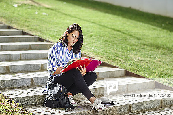 Student sitzt auf einer Treppe im Freien und macht Notizen in einem Notizbuch