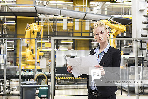 Woman holding plan in factory shop floor with industrial robot