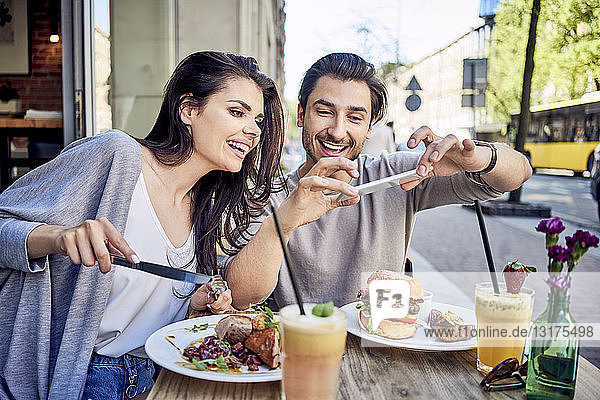 Happy young couple taking photo of food at outdoors restaurant