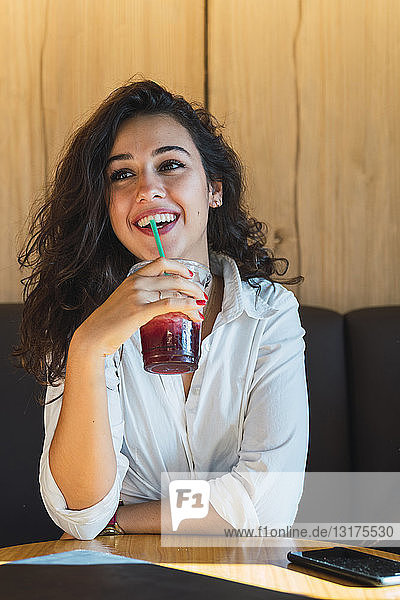 Porträt einer glücklichen jungen Frau  die einen Smoothie trinkt