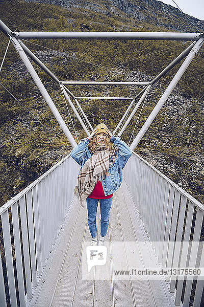 Junge Frau steht auf einer windigen Brücke und hält ihre Mütze