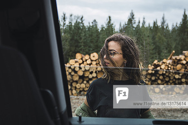 Junge Frau steht neben dem Auto neben einem Holzstapel