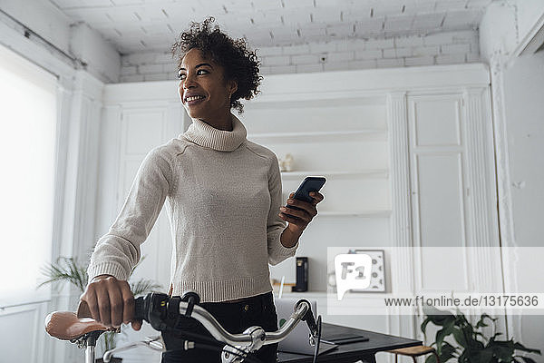 Mid adult woman leaving her home office  pushing bicycle  using smartphone
