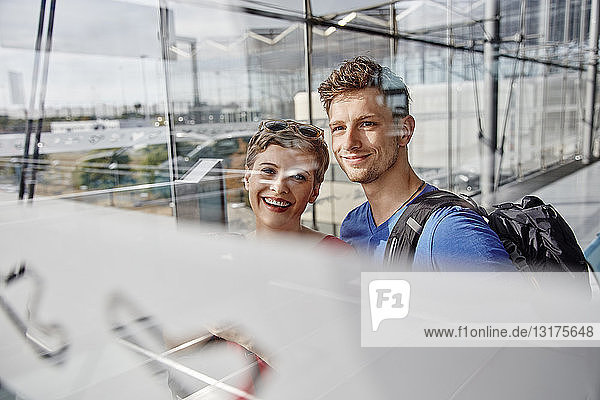 Porträt eines lächelnden Paares auf dem Flughafen,  das aus dem Fenster schaut