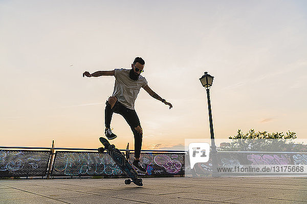 Junger Mann macht in der Stadt bei Sonnenuntergang einen Skateboardtrick