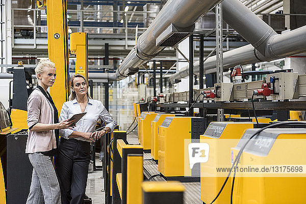 Zwei Frauen mit Tablette schauen auf die Maschine in der Fabrikhalle