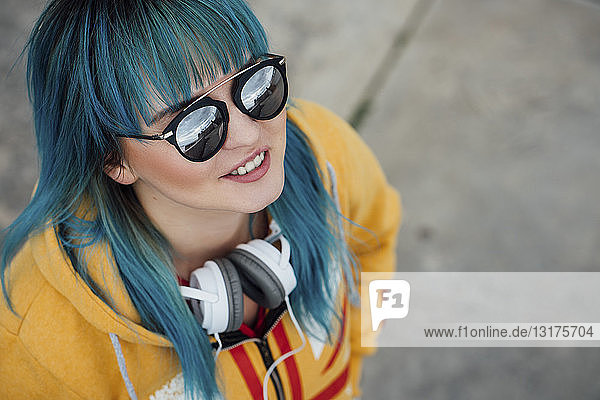 Porträt einer jungen Frau mit blau gefärbten Haaren und Kopfhörern nach oben blickend
