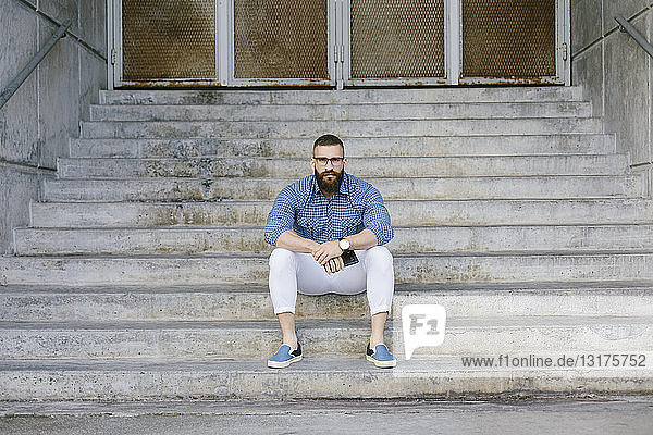 Porträt eines bärtigen Hipster-Geschäftsmannes mit Smartphone auf der Treppe sitzend
