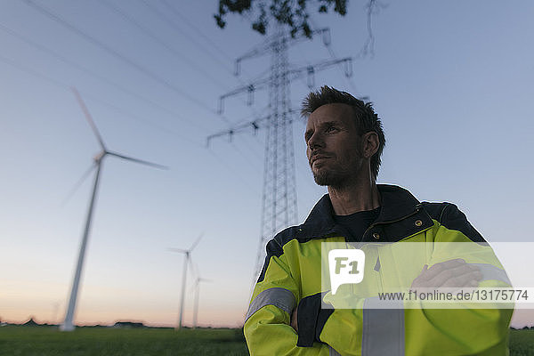 Porträt eines Ingenieurs neben einem Windpark und Strommast