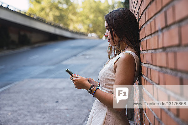 Junge Frau vor einer Ziegelmauer mit Smartphone