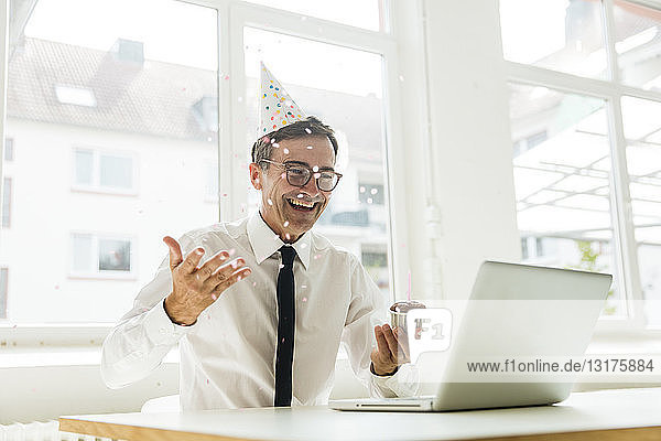Lachender Geschäftsmann mit Laptop feiert Geburtstag im Amt