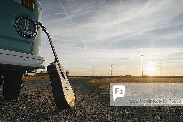 An ein Wohnmobil gelehnte Gitarre in ländlicher Landschaft mit Windturbinen bei Sonnenuntergang
