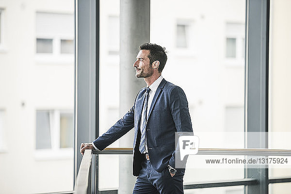 Successful businessman standing in office building  looking out of window  daydreaming