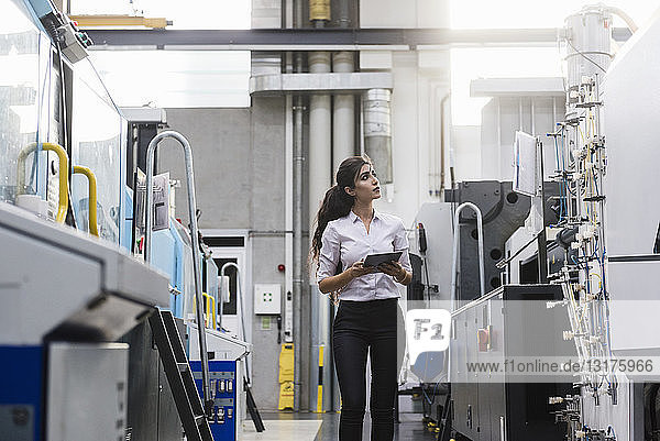 Woman with tablet at machine in factory shop floor lookig around