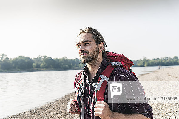 Selbstbewusster junger Mann mit Rucksack am Flussufer