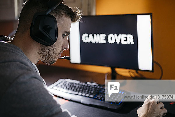 Junger Mann sitzt an seinem PC und schaut auf Bildschirm mit Spiel über Text