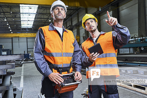 Two men in factory talking and operating machinery with remote console