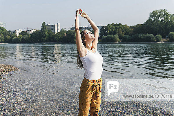 Glückliche junge Frau steht entspannt am Flussufer