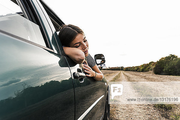 Young woman leaning out of car window on dirt track