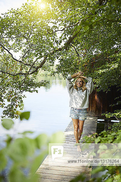Lächelnde Frau steht auf einem Holzsteg an einem abgelegenen See