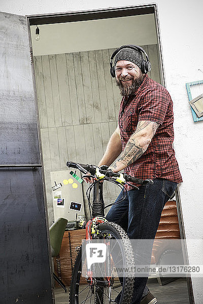 Portrait of happy man with bicycle wearing headphones in office