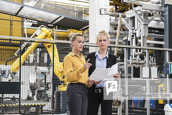 Zwei Frauen diskutieren Plan in Fabrikhalle mit Industrieroboter