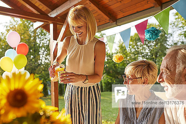 Glückliche Frau serviert Saft auf einer Gartenparty
