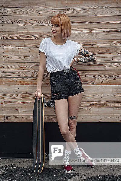Junge Frau steht an Holzwand mit Schnitzerin Skateboard