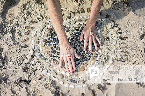 Reife Frau macht am Strand ein Herz aus Muscheln