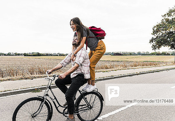 Glückliches junges Paar fährt gemeinsam auf einem Fahrrad auf der Landstraße