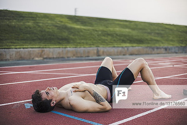 Athlete lying resting on a tartan track after finishing a race