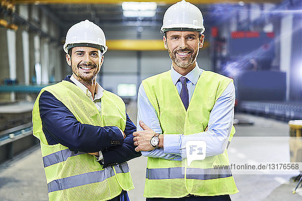 Porträt von zwei lächelnden Managern mit Arbeitsschutzkleidung in der Fabrik