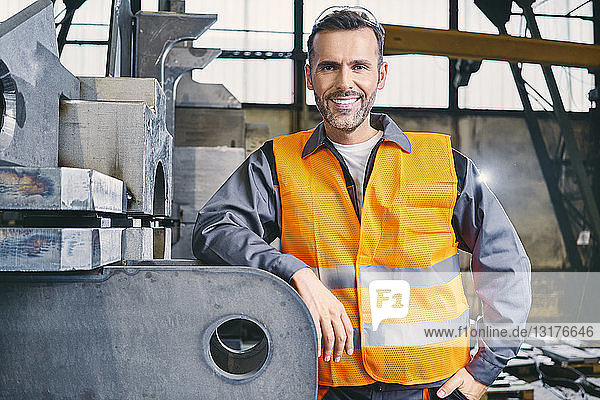 Porträt eines lächelnden Mannes mit Arbeitsschutzkleidung in der Fabrik
