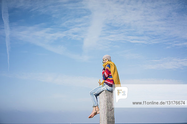 Reife Frau sitzt auf einem Holzpfahl am Strand