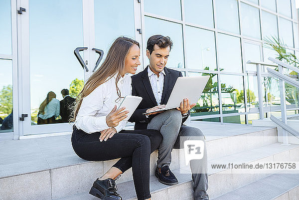 Geschäftsfrau und Geschäftsmann arbeiten mit Tablet und Laptop vor dem Bürogebäude