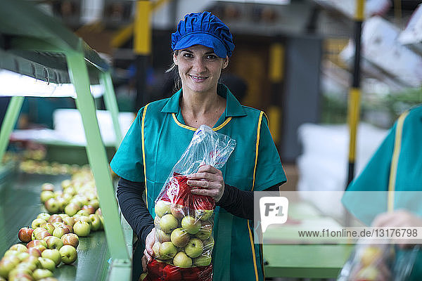 Porträt einer lächelnden Frau  die in der Fabrik Äpfel in Plastiktüten hält