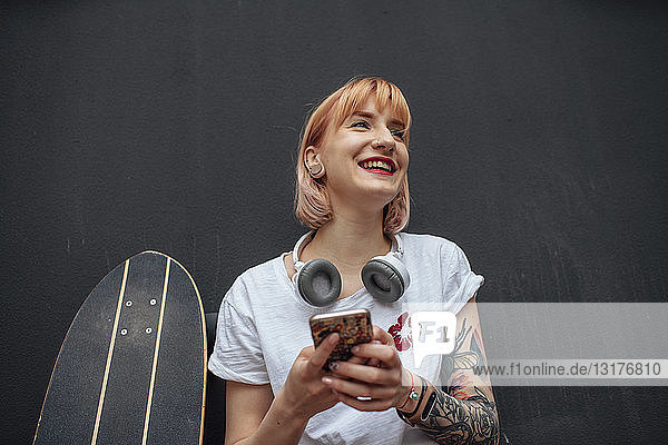 Happy young woman with skateboard  headphones and cell phone