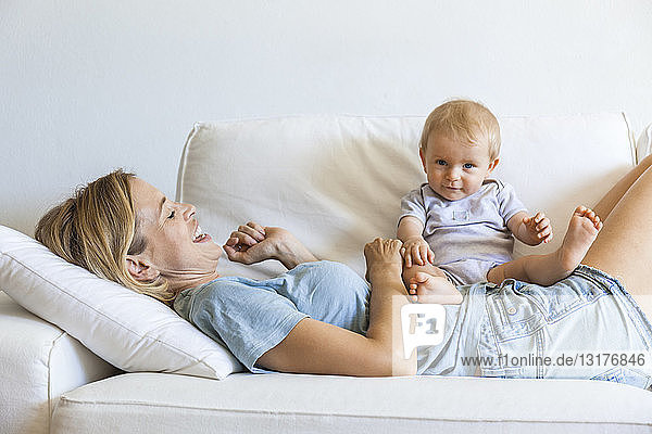 Glückliche Mutter liegt mit ihrem kleinen Mädchen auf der Couch