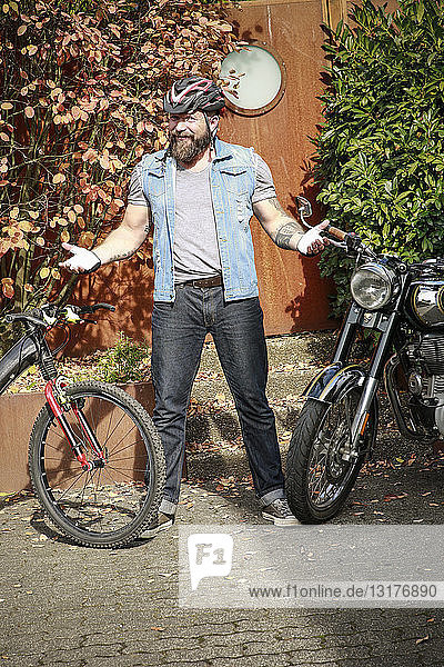 Porträt eines Mannes  der zwischen Motorrad und Fahrrad steht