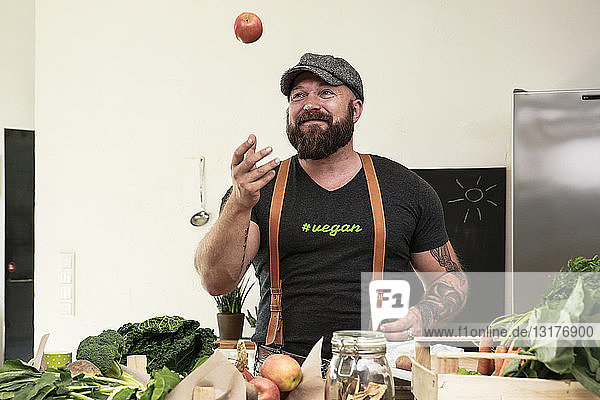 Veganer  der in seiner Küche mit Äpfeln jongliert