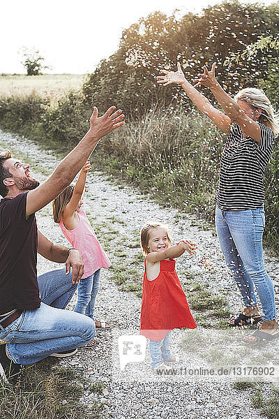 Glückliche Familie mit zwei Töchtern  die auf einem Feldweg mit Konfetti spielen