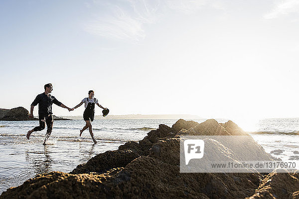 Frankreich  Bretagne  glückliches junges Paar läuft Hand in Hand am Strand