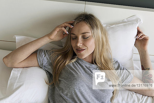 Lächelnde blonde junge Frau liegt im Bett