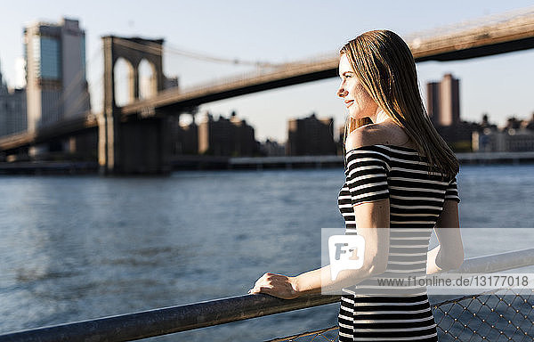 USA  New York  Brooklyn  woman wearing striped dress standing in front of East River by sunset