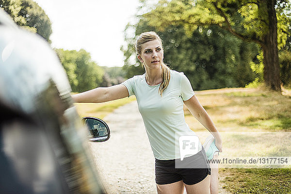 Sportive young woman stretching at a car in a park