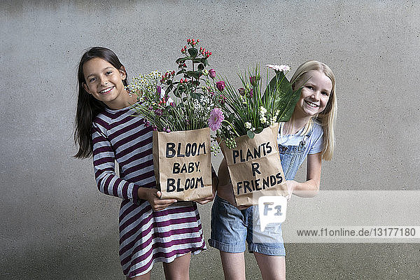 Porträt von zwei lächelnden Mädchen  die Papiertüten mit Blumen halten