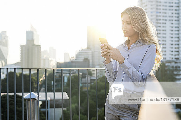 Blonde business woman checking smartphone on city rooftop