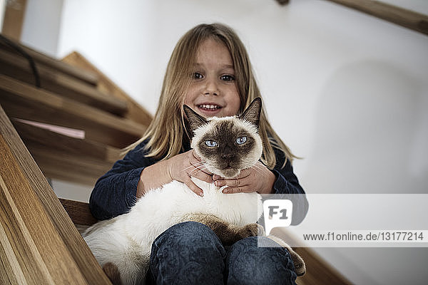Kleines Mädchen sitzt mit ihrer Siamkatze zu Hause auf der Treppe