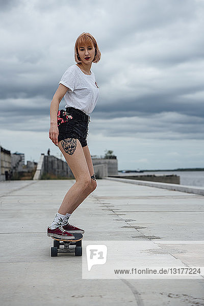 Junge Frau fährt Carver-Skateboard am Flussufer